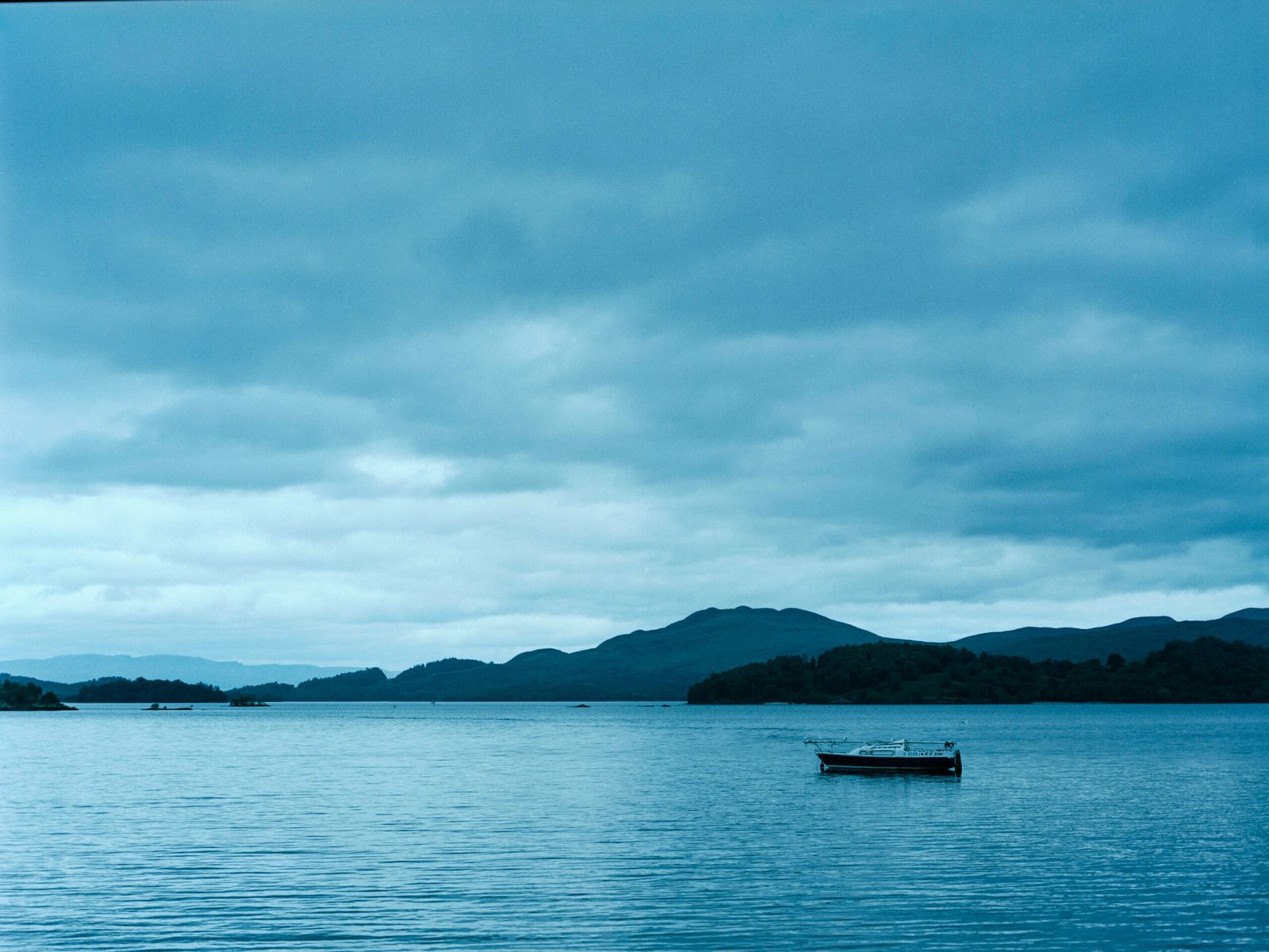 boat on sea near mountain under cloudy sky during daytime